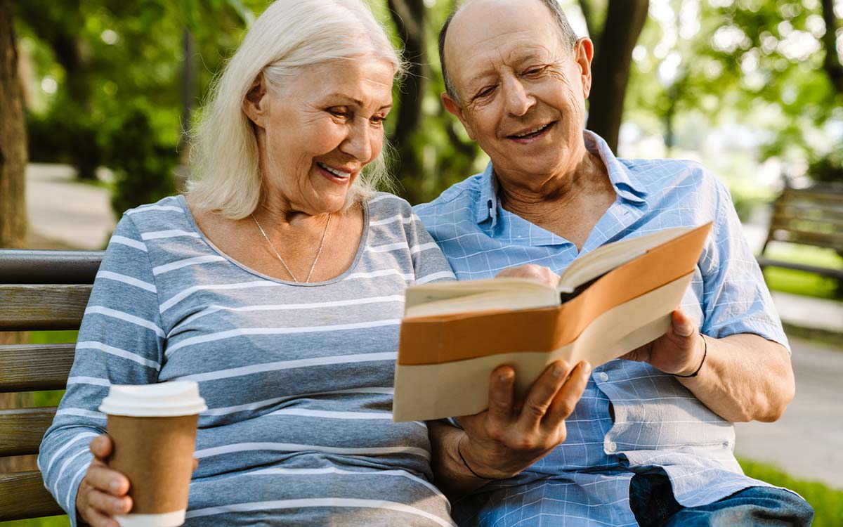 senior couple reading book on park bench how to retire well